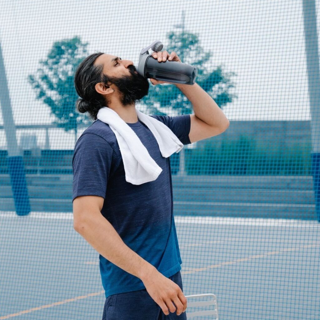 man on tennis court chugging water from water bottle
